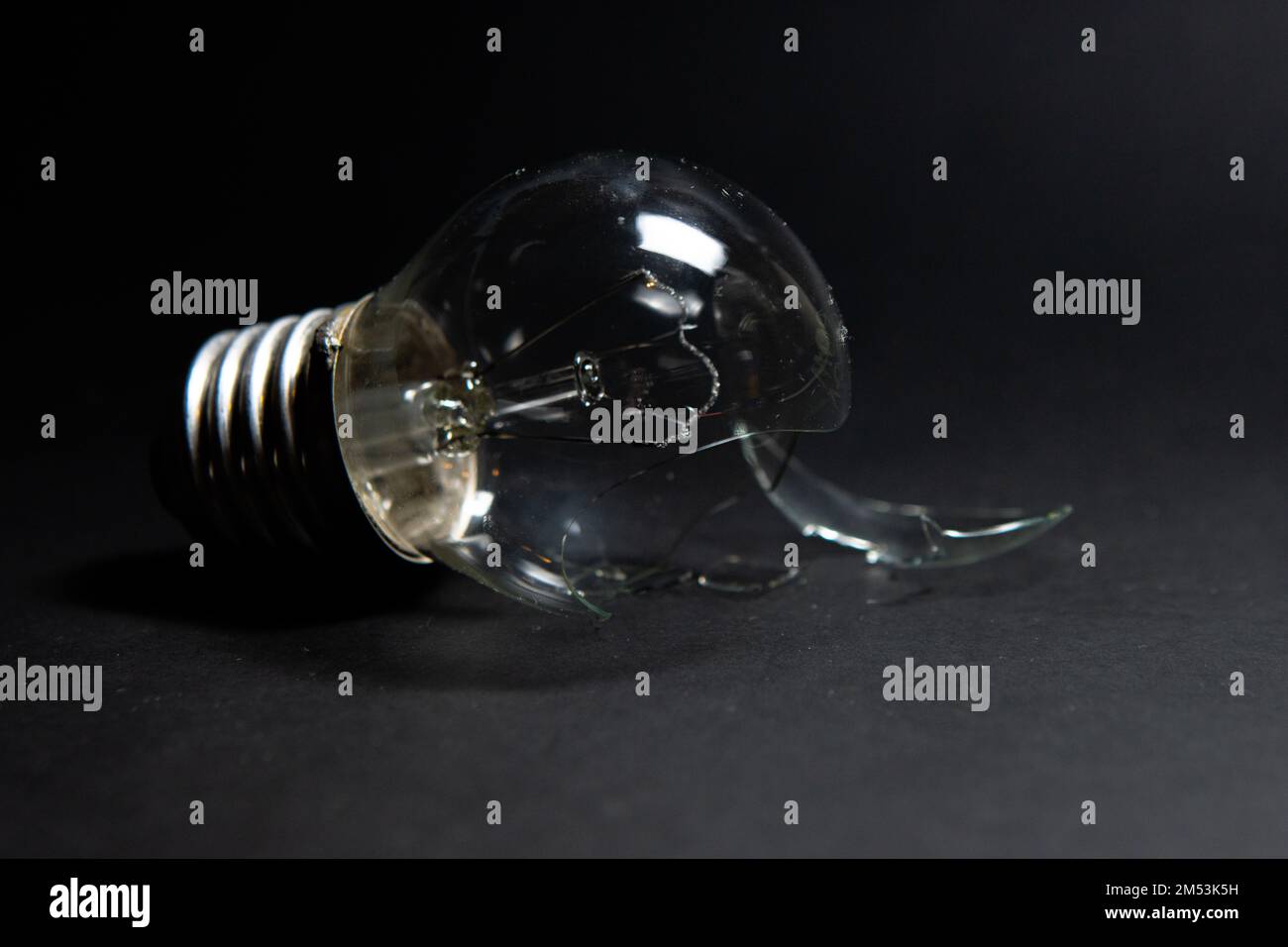 Gebrochene Glühlampe mit Glasscherben auf schwarzem Hintergrund. Das Konzept der Strompreise und die Stromversorgungskrise Stockfoto