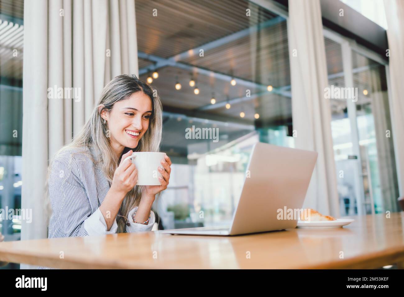 Ruhige Geschäftsfrau der Millennials, die ein Notebook benutzt, mit einer Tasse Kaffee am modernen Arbeitsplatz. Stockfoto