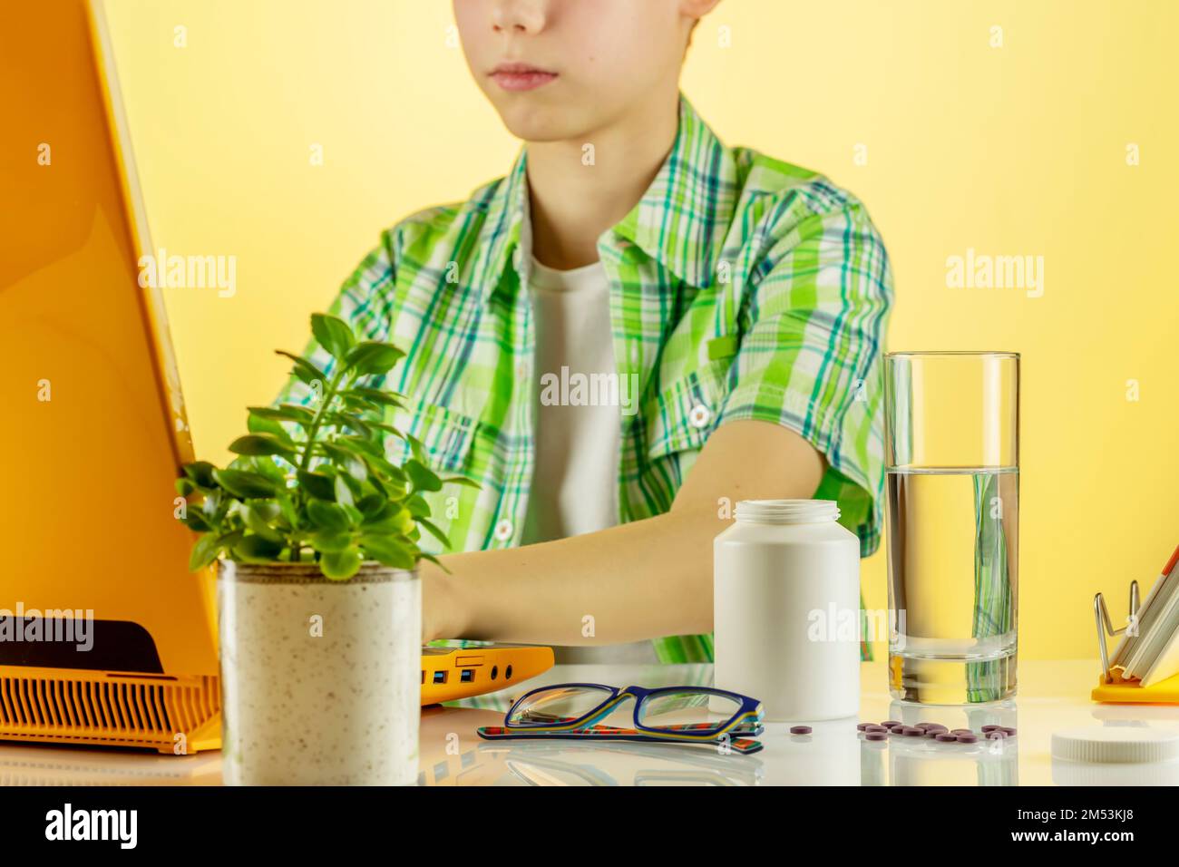 Ein Junge, der ein Notebook benutzt, zu Hause online lernt und Vitamine in Gelkapseln mit Wasser abspült. Ergänzungen von Omega 3 oder D 3 sind gut für die Gesundheit von Kindern. M Stockfoto