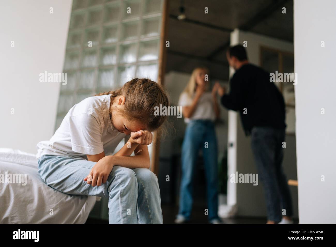 Tiefer Blickwinkel auf Verzweiflung einsames kleines Mädchen weinend Leiden sitzen auf dem Sofa während Eltern streiten und kämpfen im Wohnzimmer im Hintergrund. Stockfoto