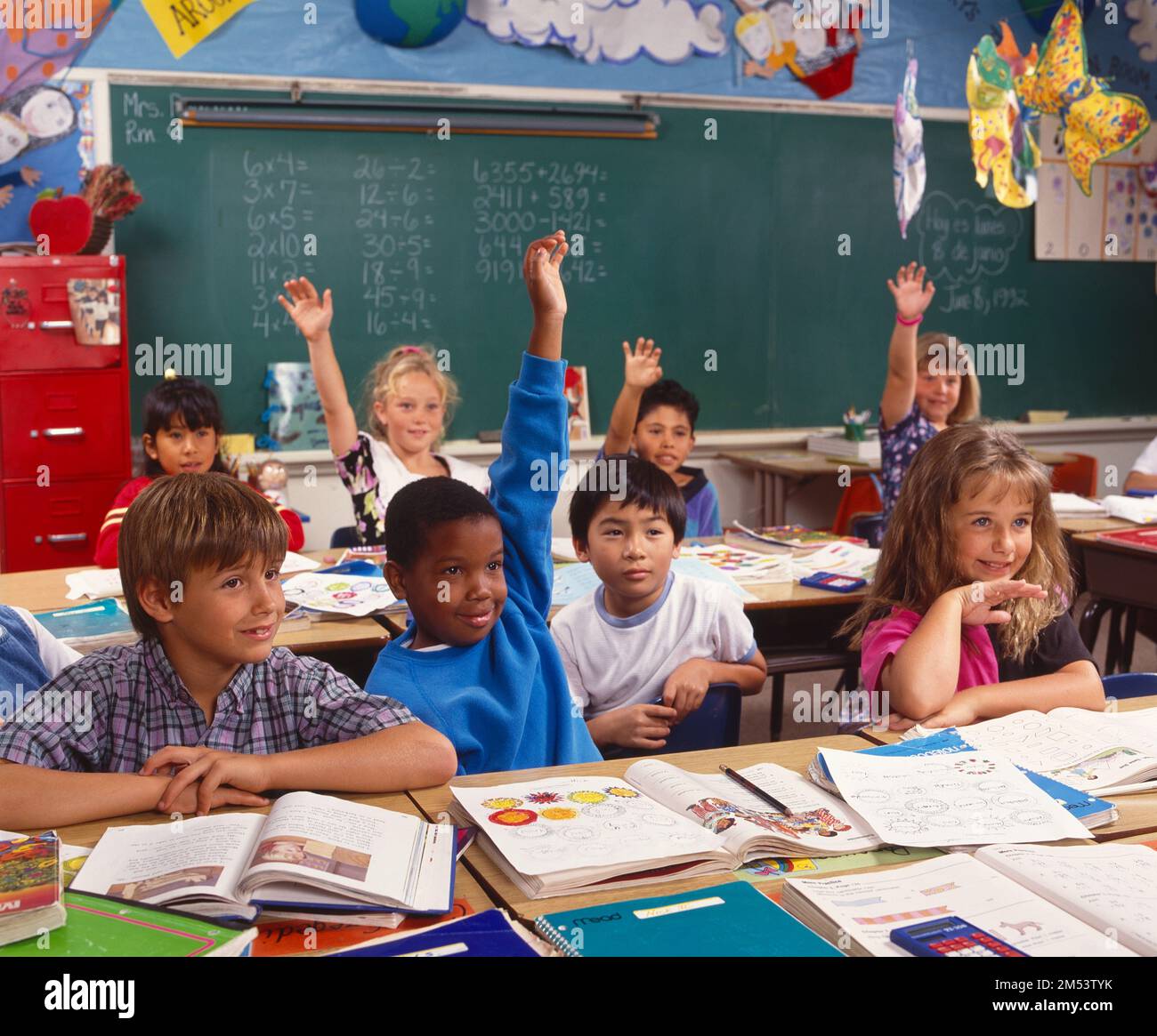 Kinder in einem Klassenzimmer, mit erhobenen Armen, um vom Lehrer erkannt zu werden Stockfoto