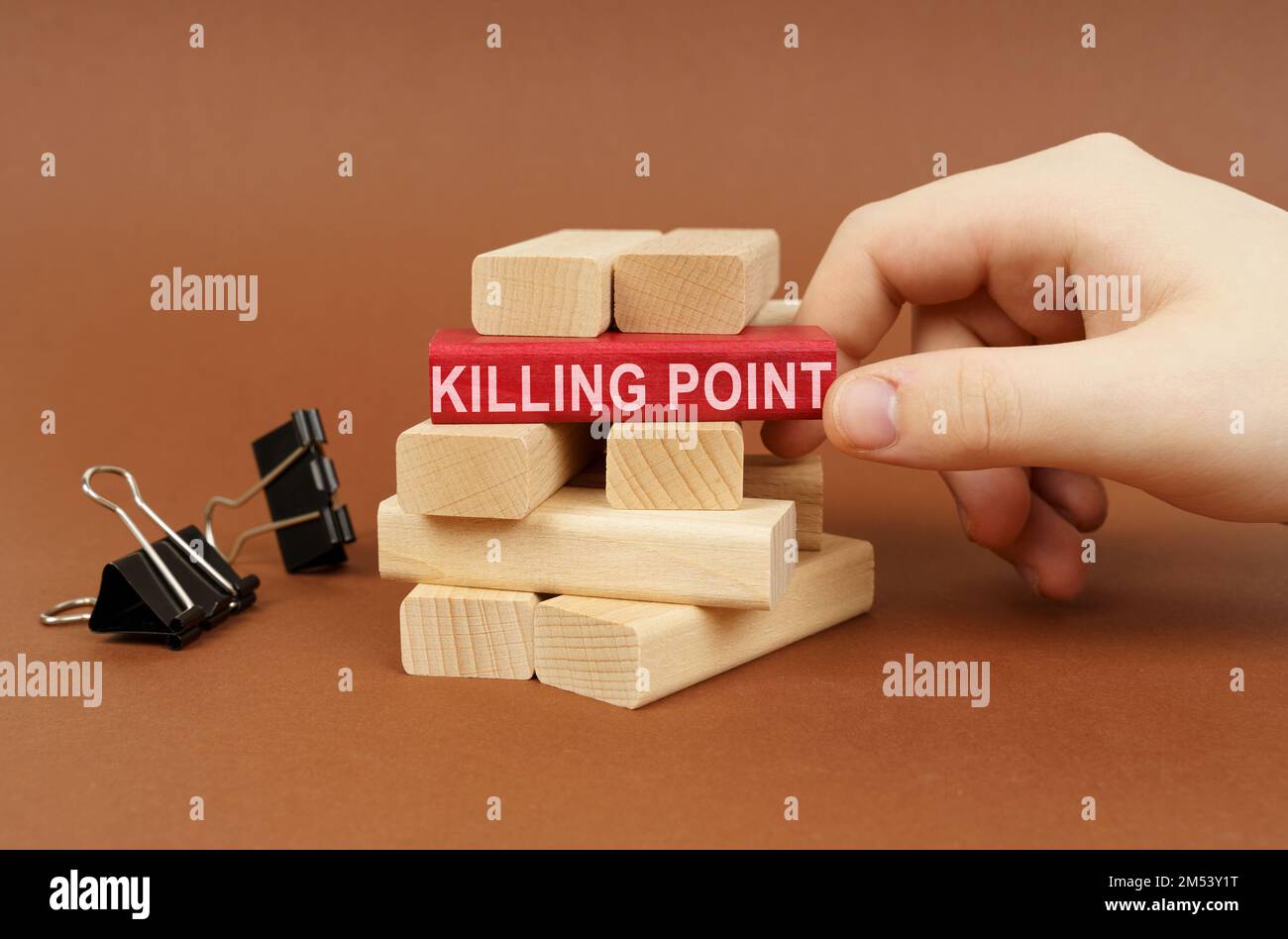 Geschäftskonzept. Klemmen und Holzblöcke liegen auf einer braunen Oberfläche, eine Person nimmt einen roten Block mit der Inschrift heraus - KILLER POINT Stockfoto