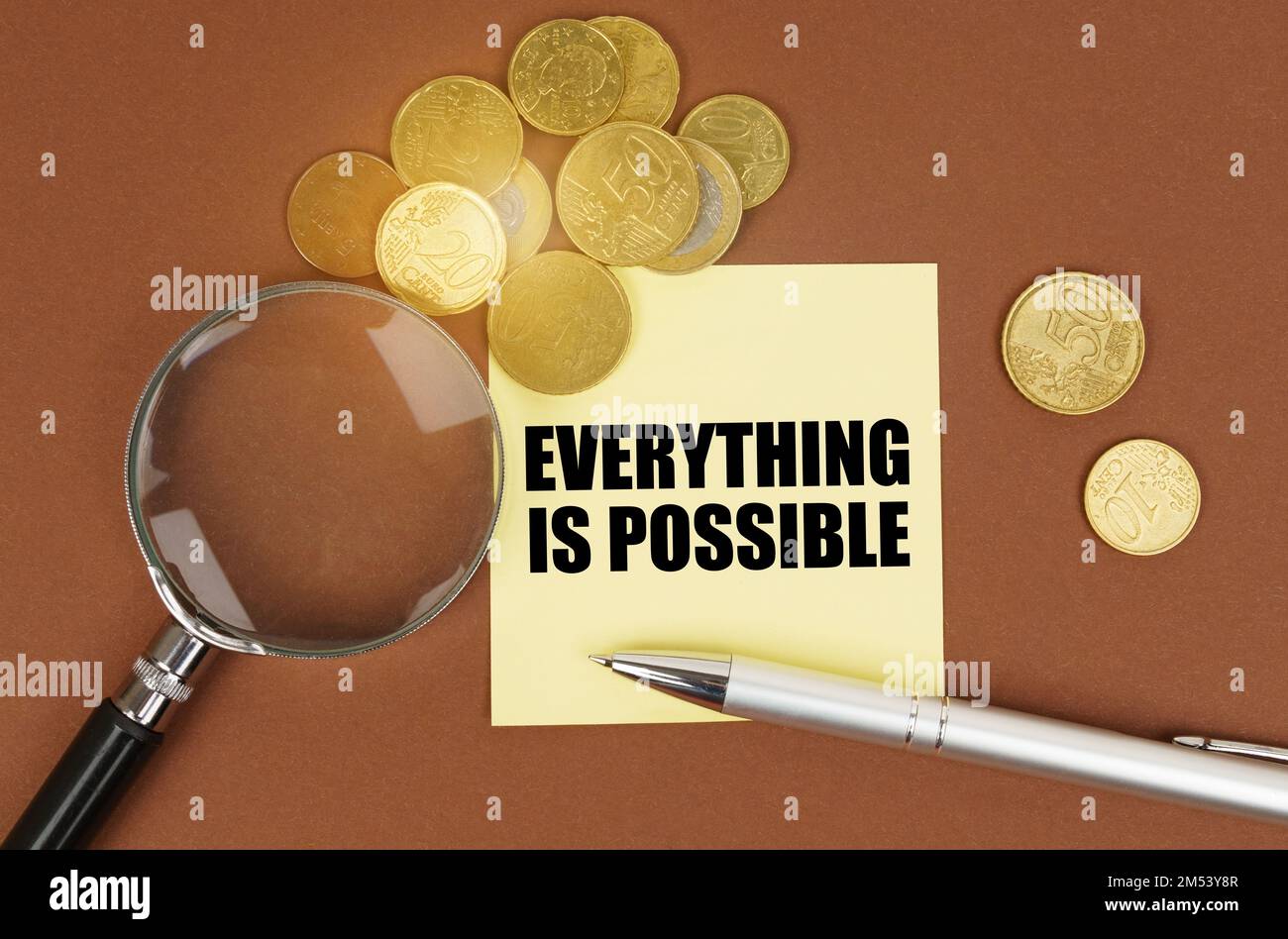 Geschäftskonzept. Auf einer braunen Oberfläche befinden sich Münzen, ein Stift, eine Lupe und Aufkleber mit der Beschriftung - alles ist möglich Stockfoto