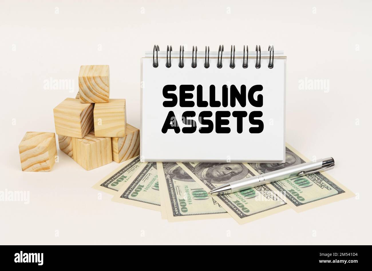 Geschäftskonzept. Auf einer weißen Oberfläche, Würfel, Dollars, ein Stift und ein Notizblock mit der Aufschrift „Selling Assets“ Stockfoto