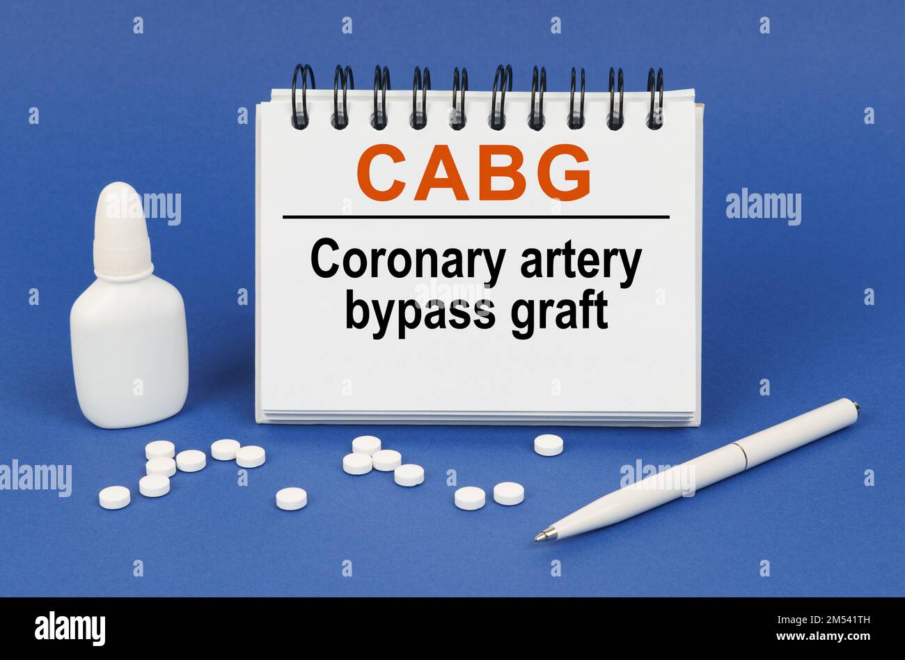 Medizinisches Konzept. Auf blauem Hintergrund einen Stift, Tabletten und einen Notizblock mit der Aufschrift „CABG koronarer Bypass“ Stockfoto