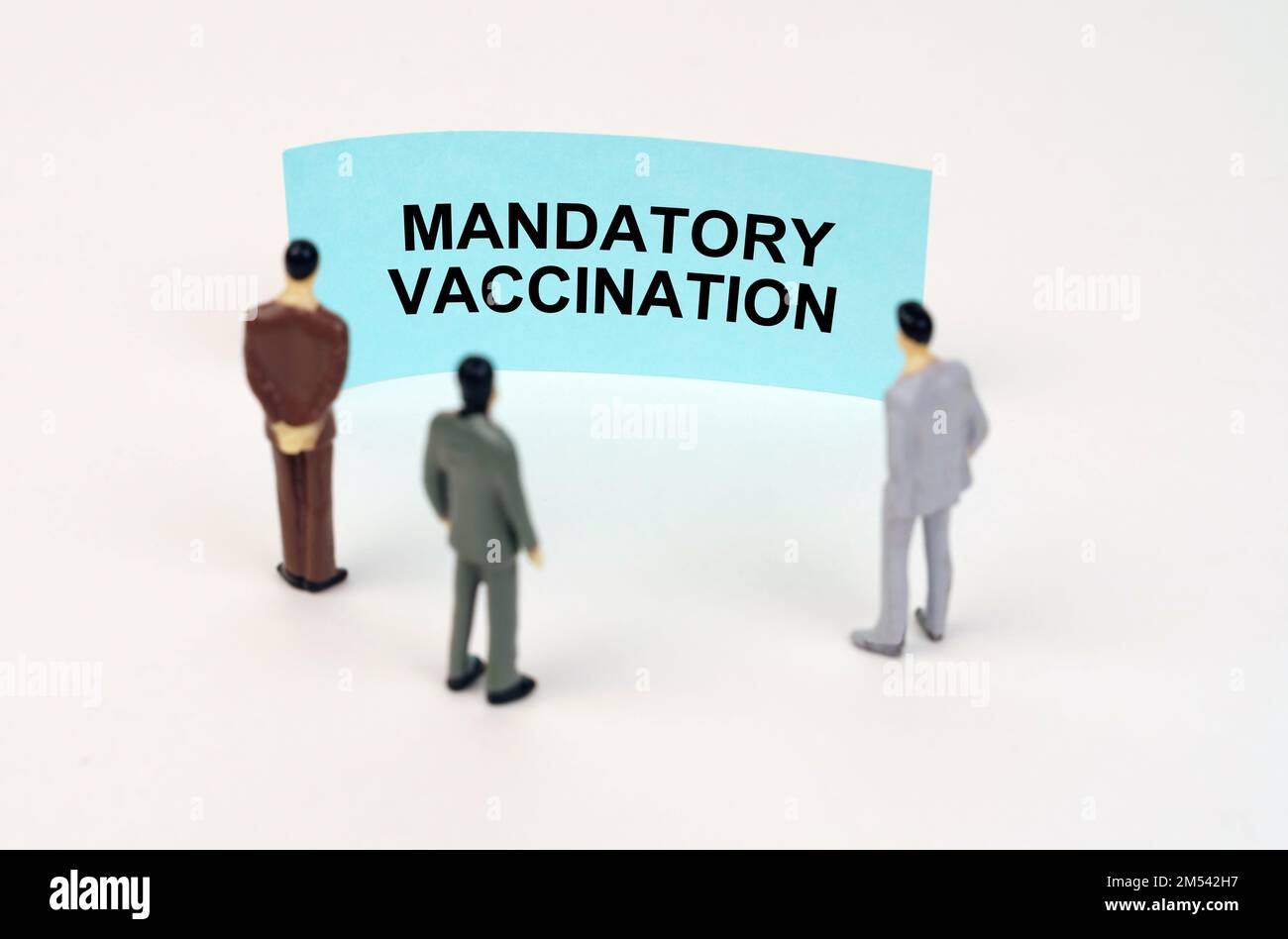Medizinisches Konzept. Miniaturfiguren von Menschen stehen vor einem blauen Schild mit der Inschrift - obligatorische Impfung Stockfoto
