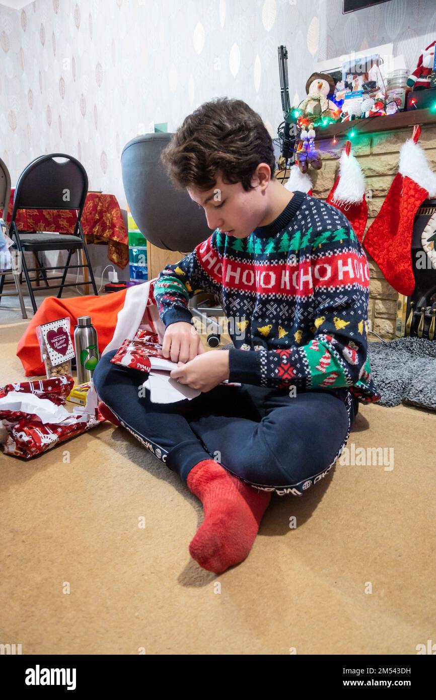 Ein Junge saß auf dem Boden und öffnete Weihnachtsgeschenke am ersten Weihnachtsfeiertag Stockfoto