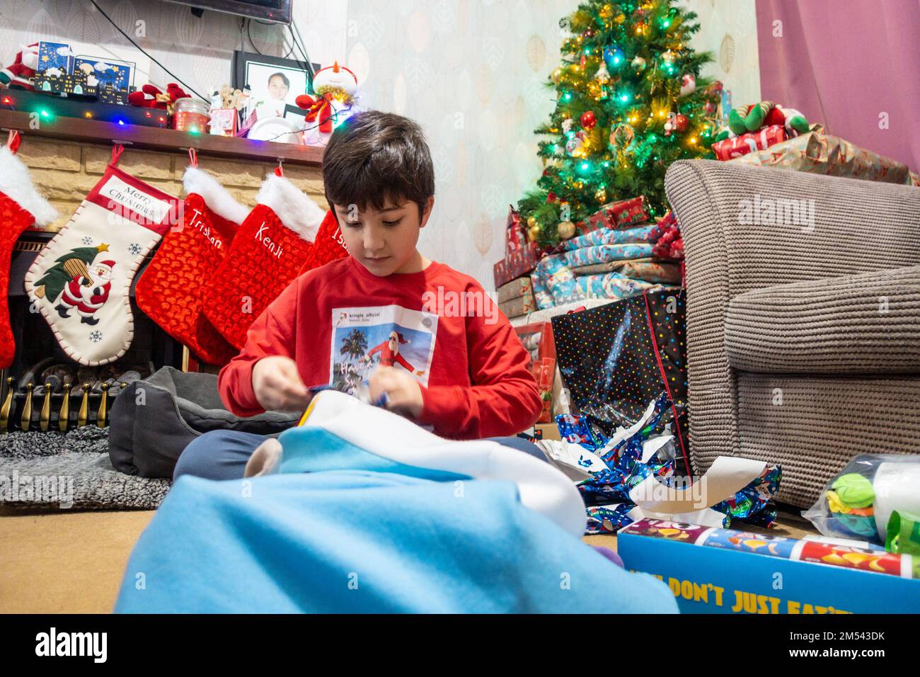 Ein Junge saß auf dem Boden und öffnete Weihnachtsgeschenke am ersten Weihnachtsfeiertag Stockfoto