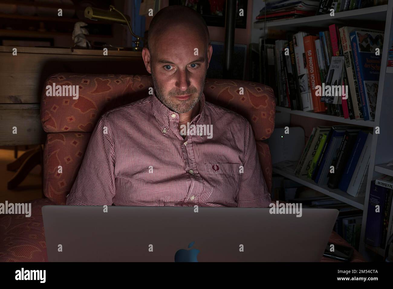 Mann sitzt im Sessel und arbeitet an seinem Laptop, Bayern, Deutschland Stockfoto