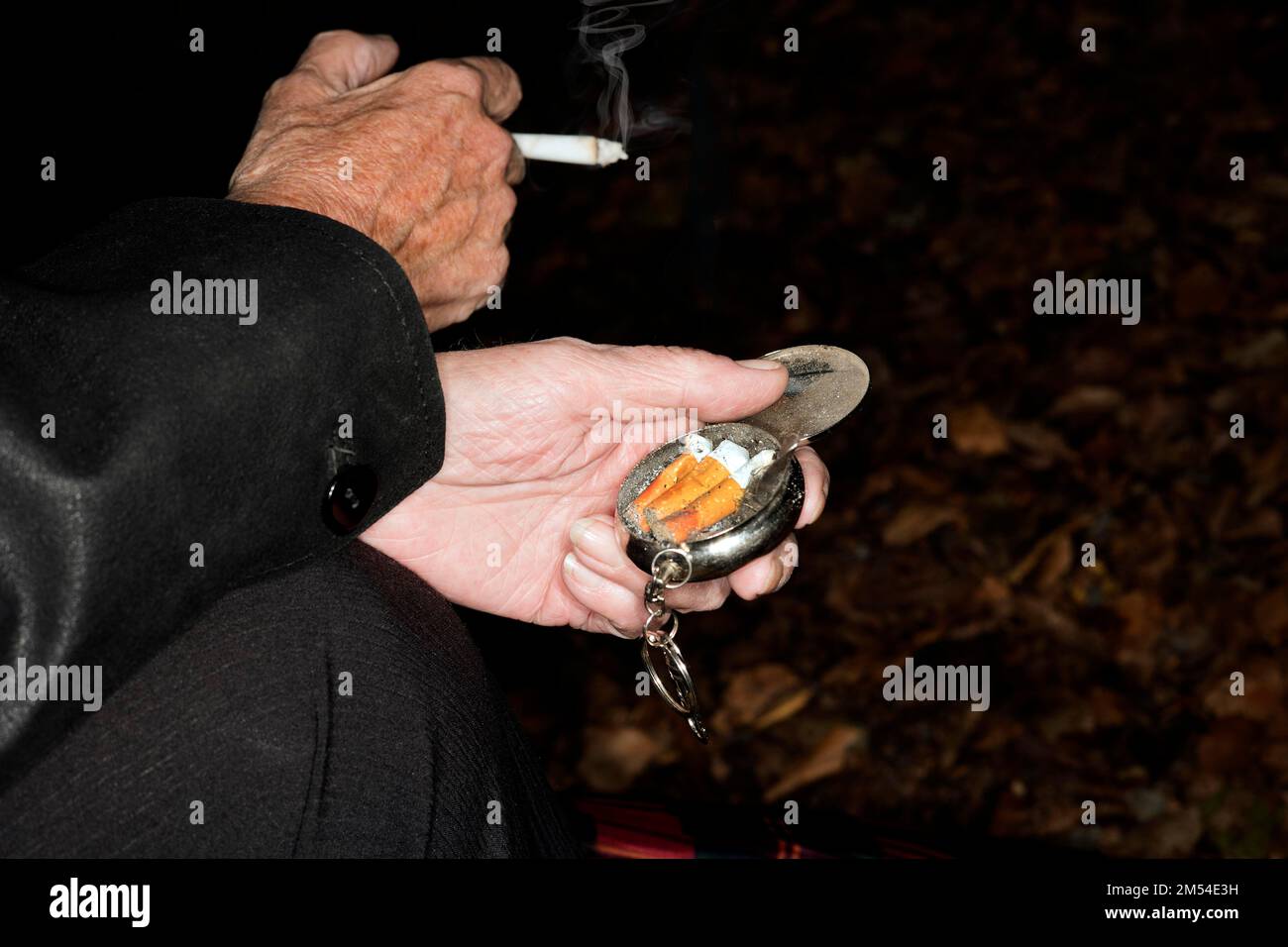 Eine Frau raucht eine Zigarette und in der linken Hand hält sie einen mobilen Aschenbecher in Berlin Stockfoto