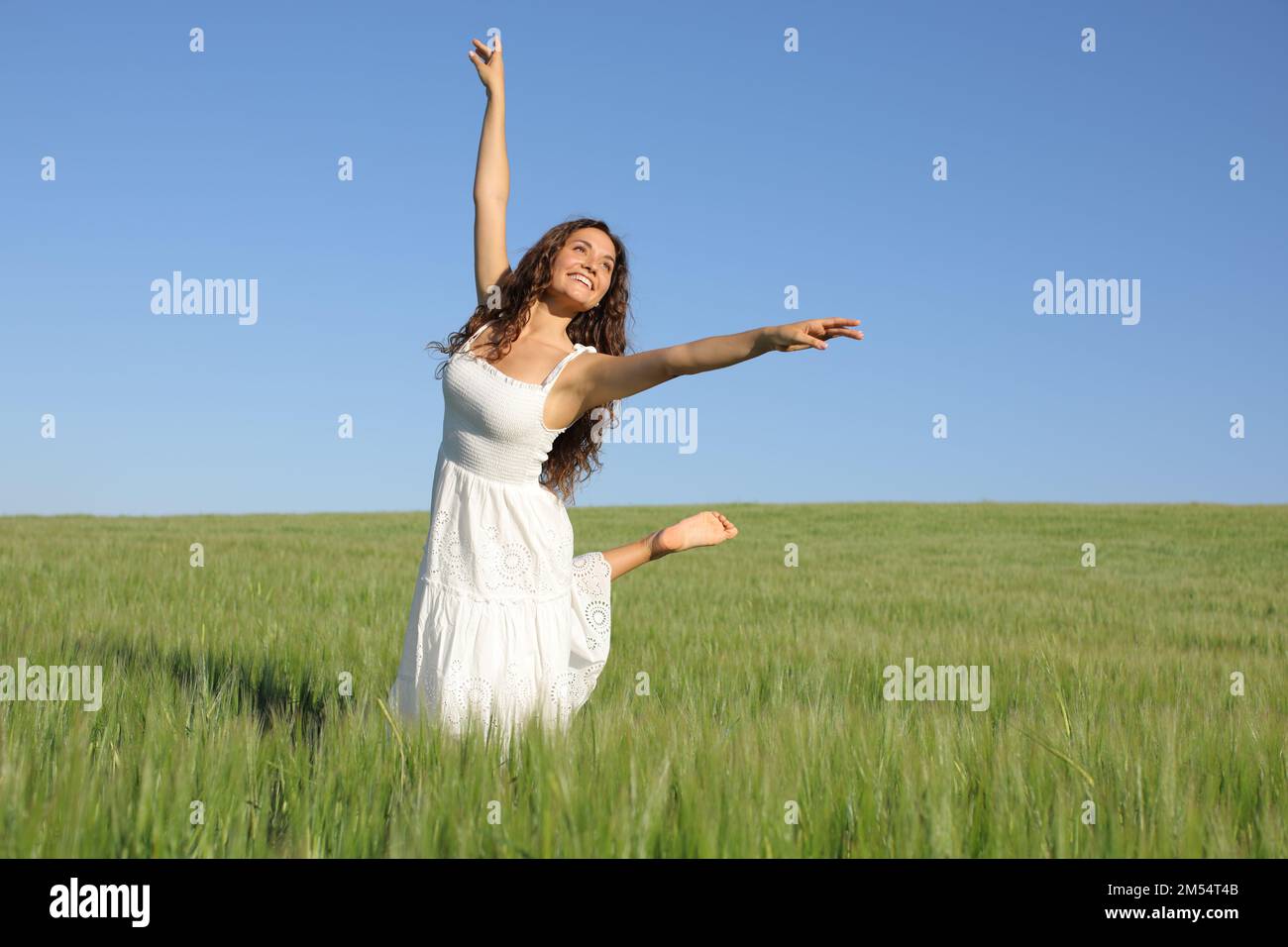 Glückliche Frau mit weißem Kleid, die auf einem grünen Weizenfeld tanzt Stockfoto
