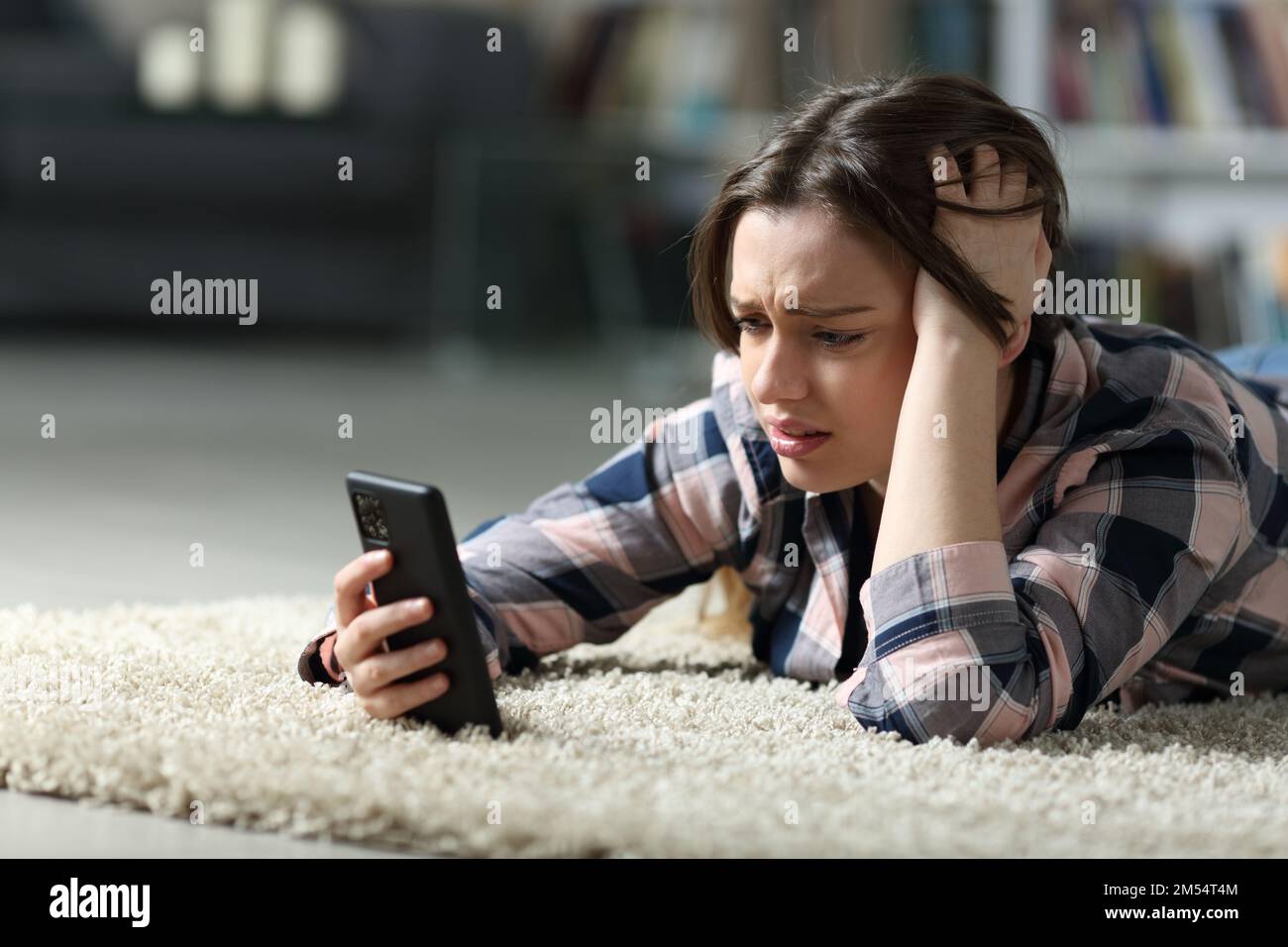 Trauriger Teenager, der nachts zu Hause sein Smartphone auf dem Boden überprüft Stockfoto