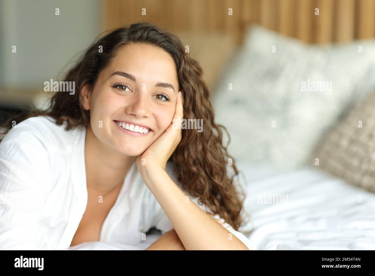 Porträt einer glücklichen Frau, die auf einem Bett in die Kamera schaut und im Schlafzimmer lächelt Stockfoto