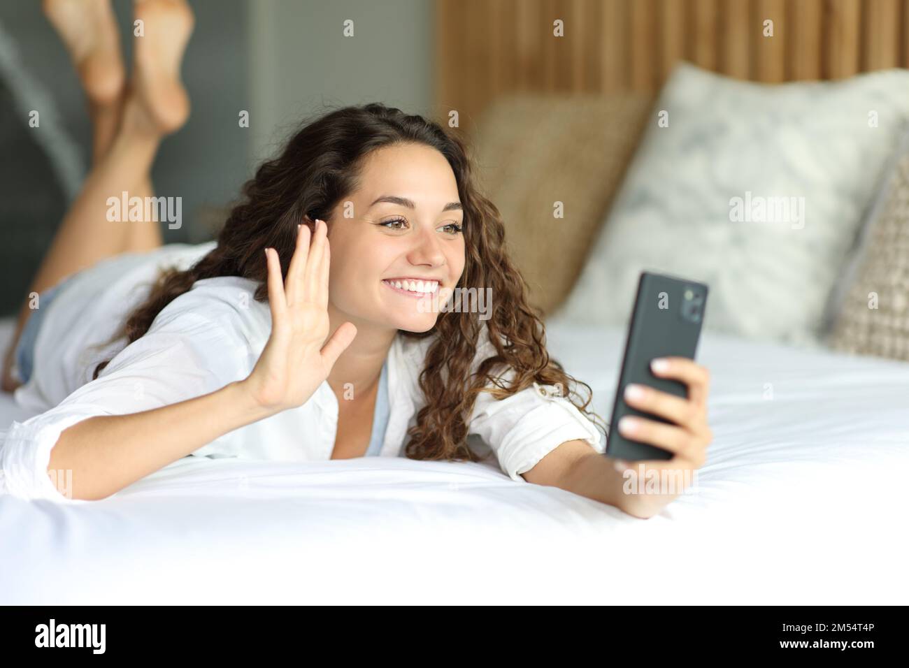 Glückliche Frau in einem Videogespräch am Telefon auf dem Bett im Schlafzimmer Stockfoto