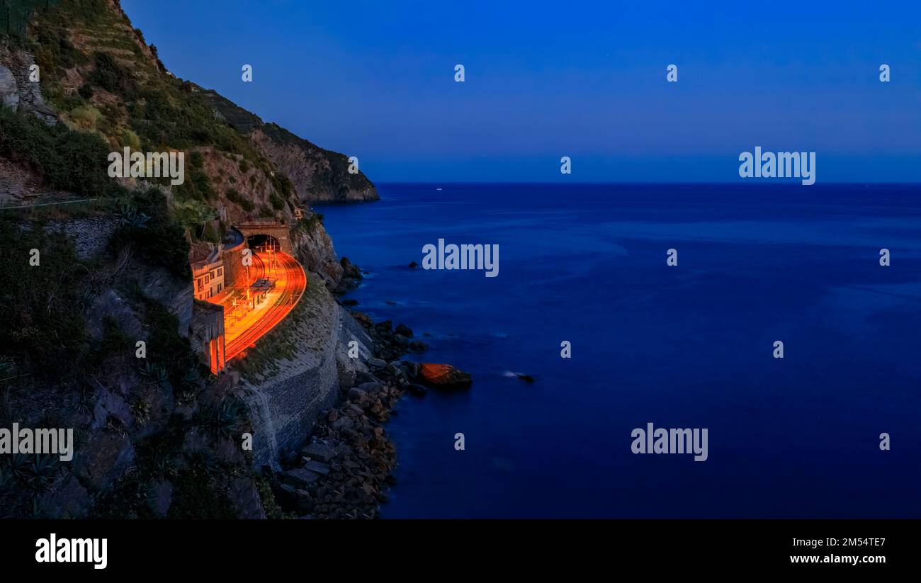 Panoramablick auf das Mittelmeer, die Klippen und die Lichter an der Zughaltestelle Manarola in Cinque Terre, Italien, bei Sonnenuntergang, lange Exposition Stockfoto