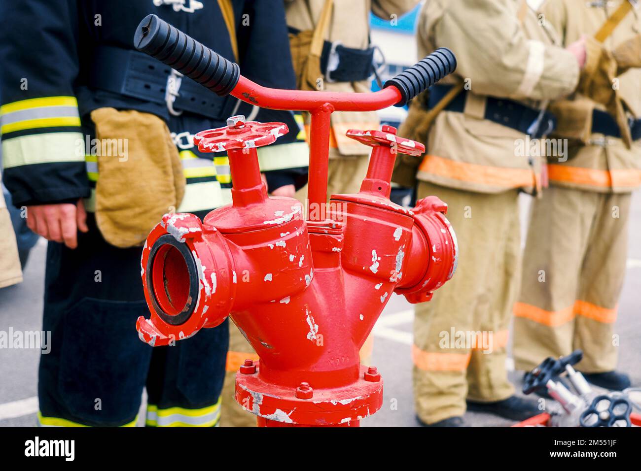 Retter stehen in Reihe. Feuerwehr vor dem Hintergrund des roten Feuerwehrkrans. Hintergrund für Rettungskräfte oder Feuerwehr. Nahaufnahme des Hydranten Stockfoto