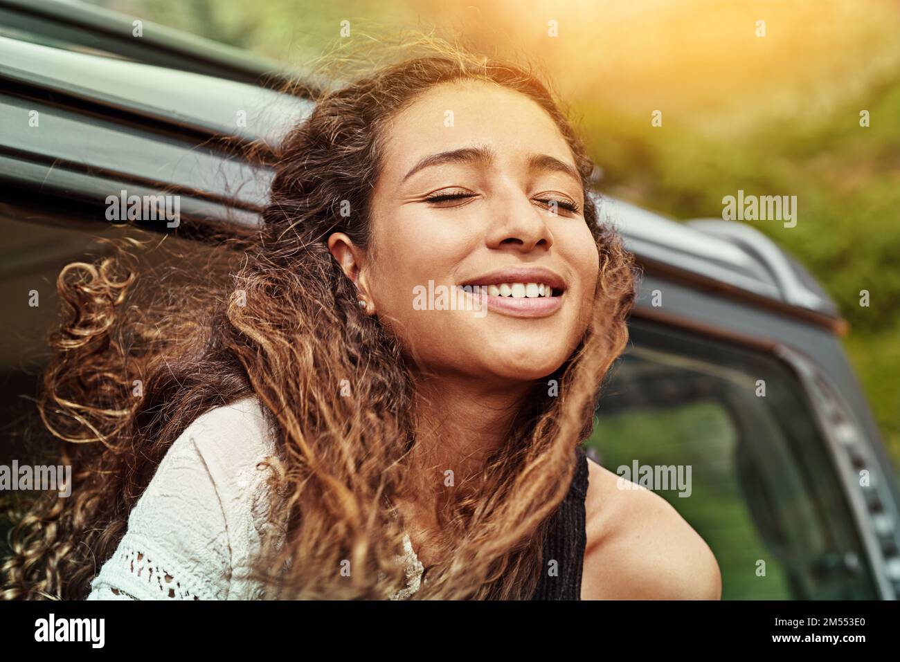 Spüren Sie den Wind in Ihren Haaren. Eine junge Frau, die sich während einer Autofahrt aus dem Fenster lehnt. Stockfoto