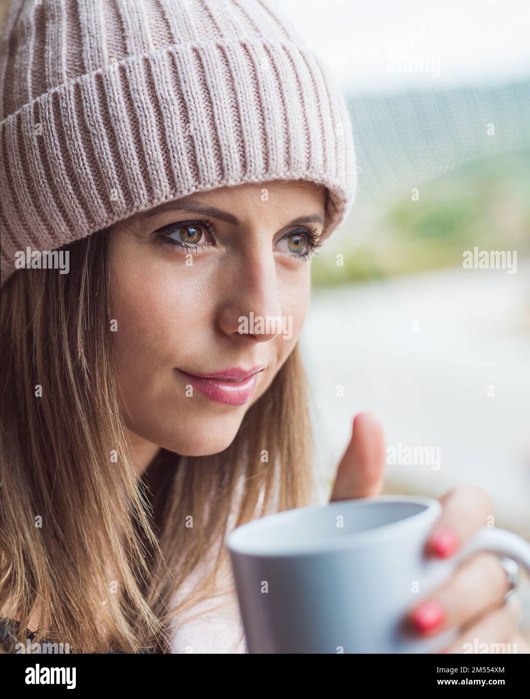 Eine Frau in einer Wollmütze, nachdenklich, in der Hand einer Tasse Kaffee. Konzept von Entspannung und Wohlbefinden. Stockfoto