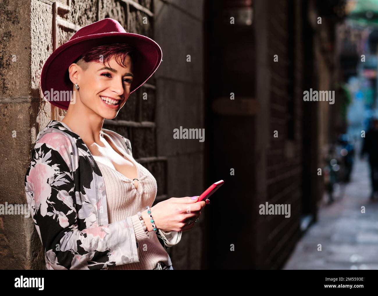Eine lächelnde Frau, die in die Kamera schaut, während sie ein Mobiltelefon im Freien benutzt Stockfoto