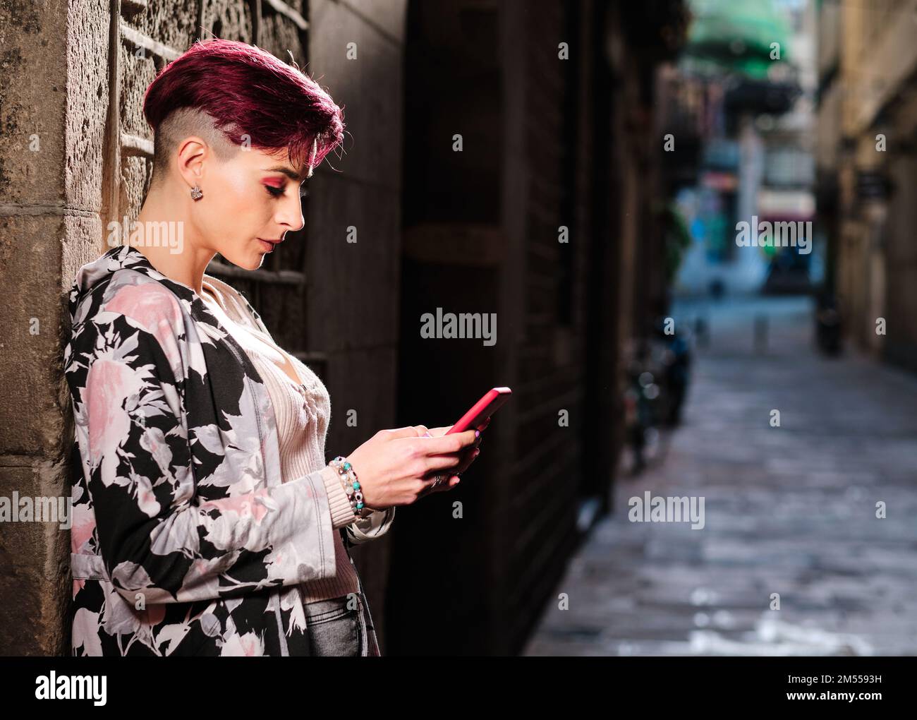 Frau mit kurzen Haaren, die ein Handy auf der Straße benutzt Stockfoto