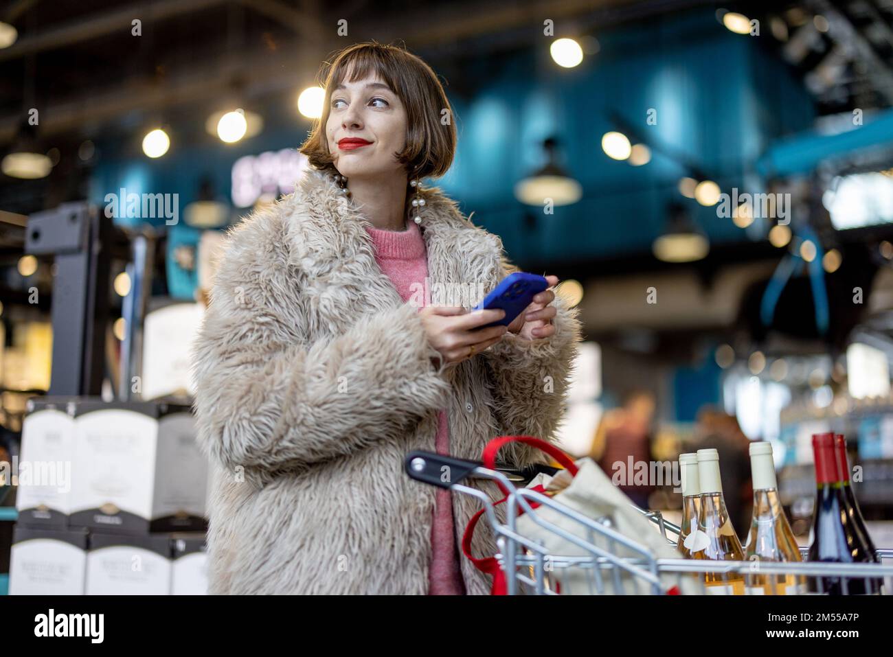 Frau mit Telefon und Wein im Supermarkt Stockfoto