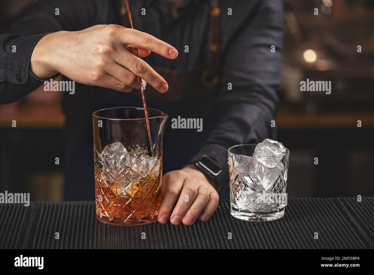 Transparentes Glas mit zerstoßenem Eis und Rum auf der Theke und eine Hand des Barkeepers, die den Cocktail darin umrührt Stockfoto