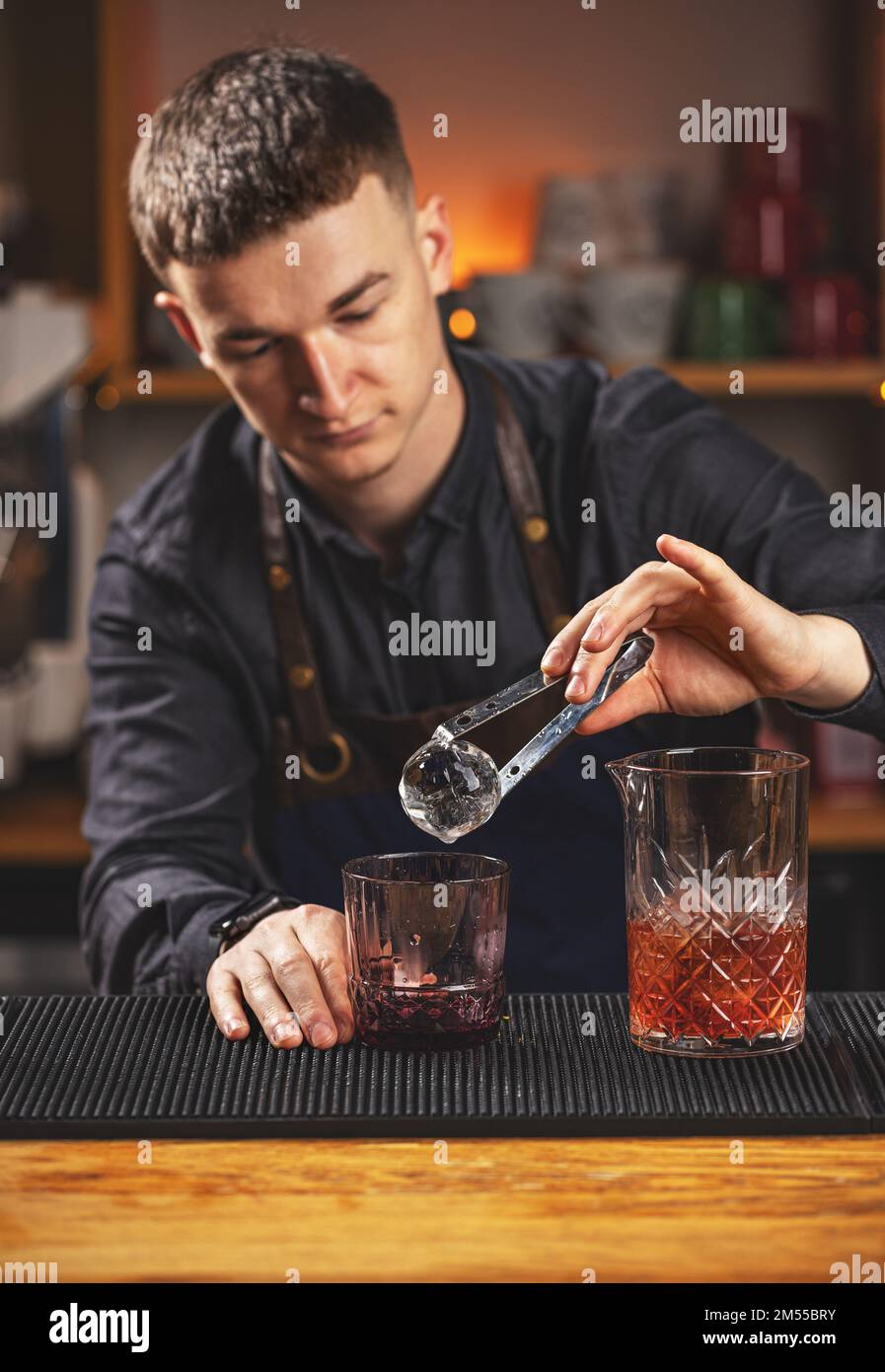 Barkeeper, der Eisball in altmodisches Glas steckt Stockfoto