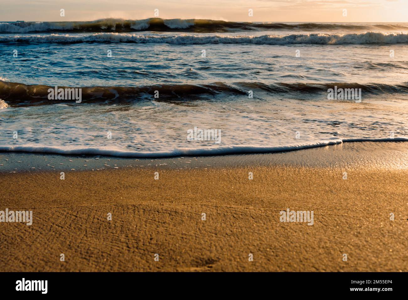 Schäumende Wellen am sonnenbeleuchteten Sandstrand am frühen Morgen im Resort Stockfoto