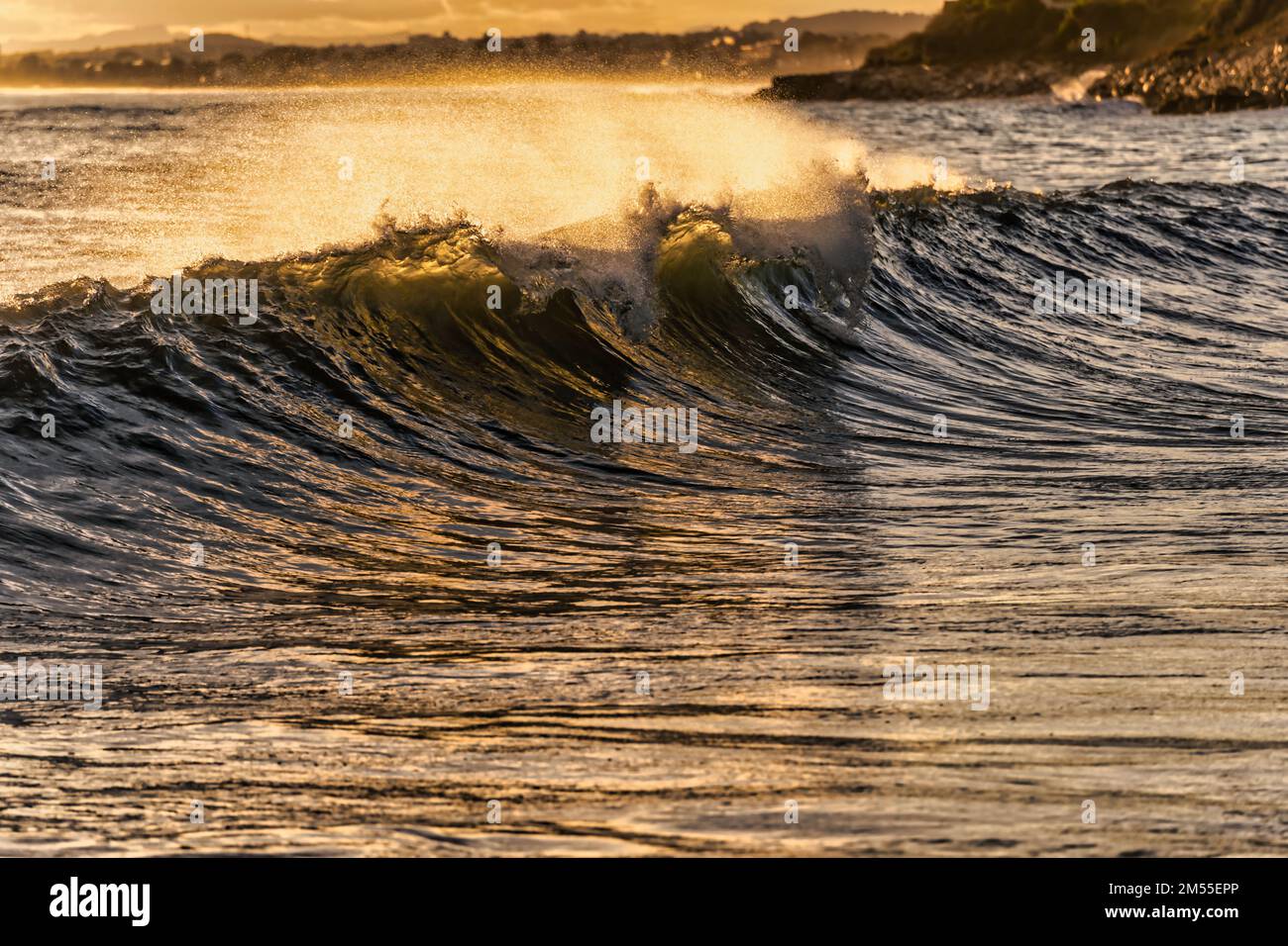 Saubere Meereswellen, die Wasser spritzen, während sie sich im Sommer bei Sonnenuntergang an der Küste entlang Rollen Stockfoto