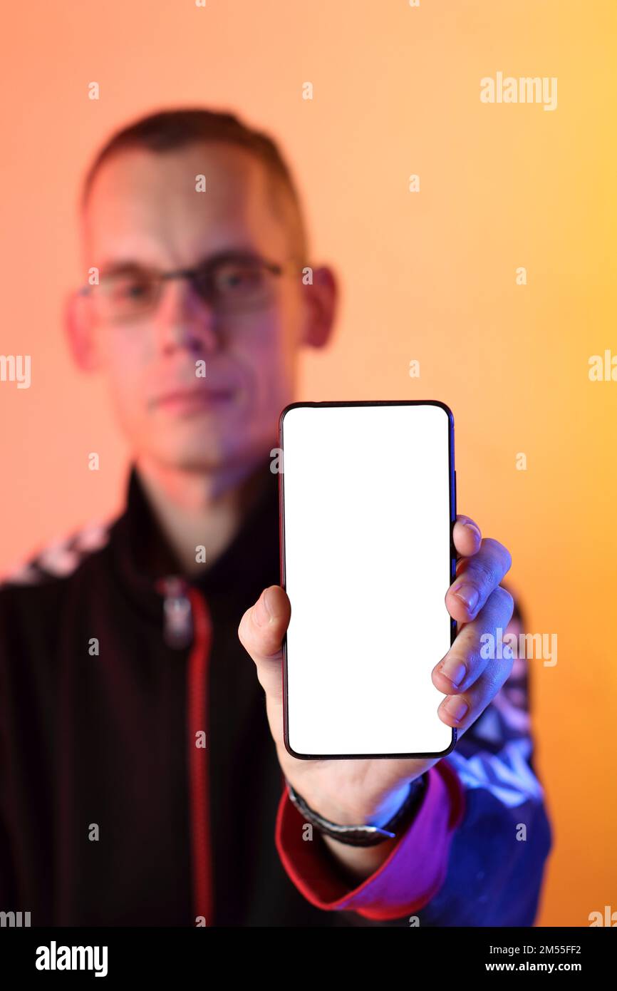 Smartphone mit einem weißen Bildschirm, der vertikal in der Hand vor dem Hintergrund einer Person und einem farbigen Hintergrund liegt Stockfoto