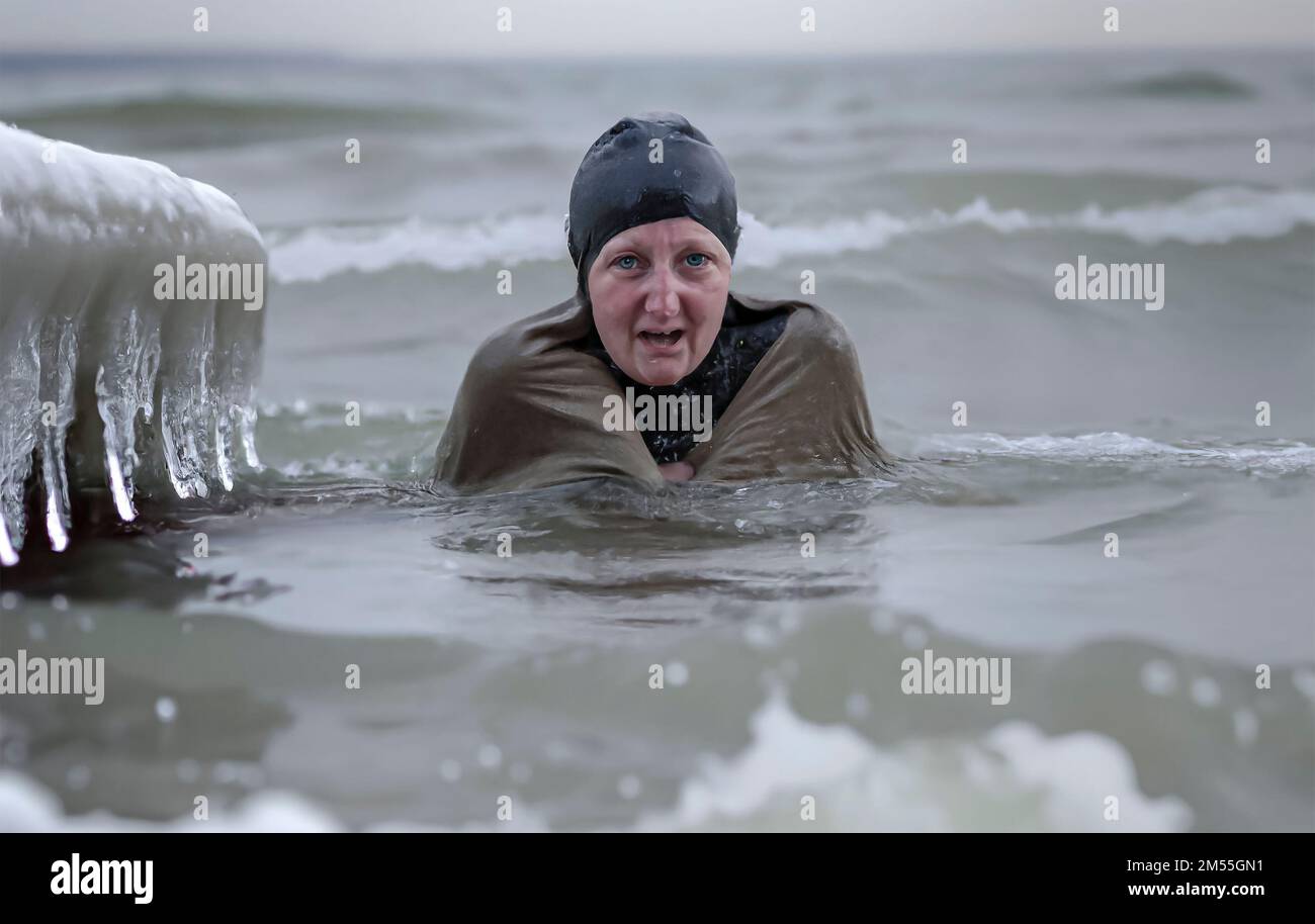 Die Frau sieht unglücklich aus, wenn sie im Meer schwimmt und Eiszapfen am Wasserrand hängen. Stockfoto