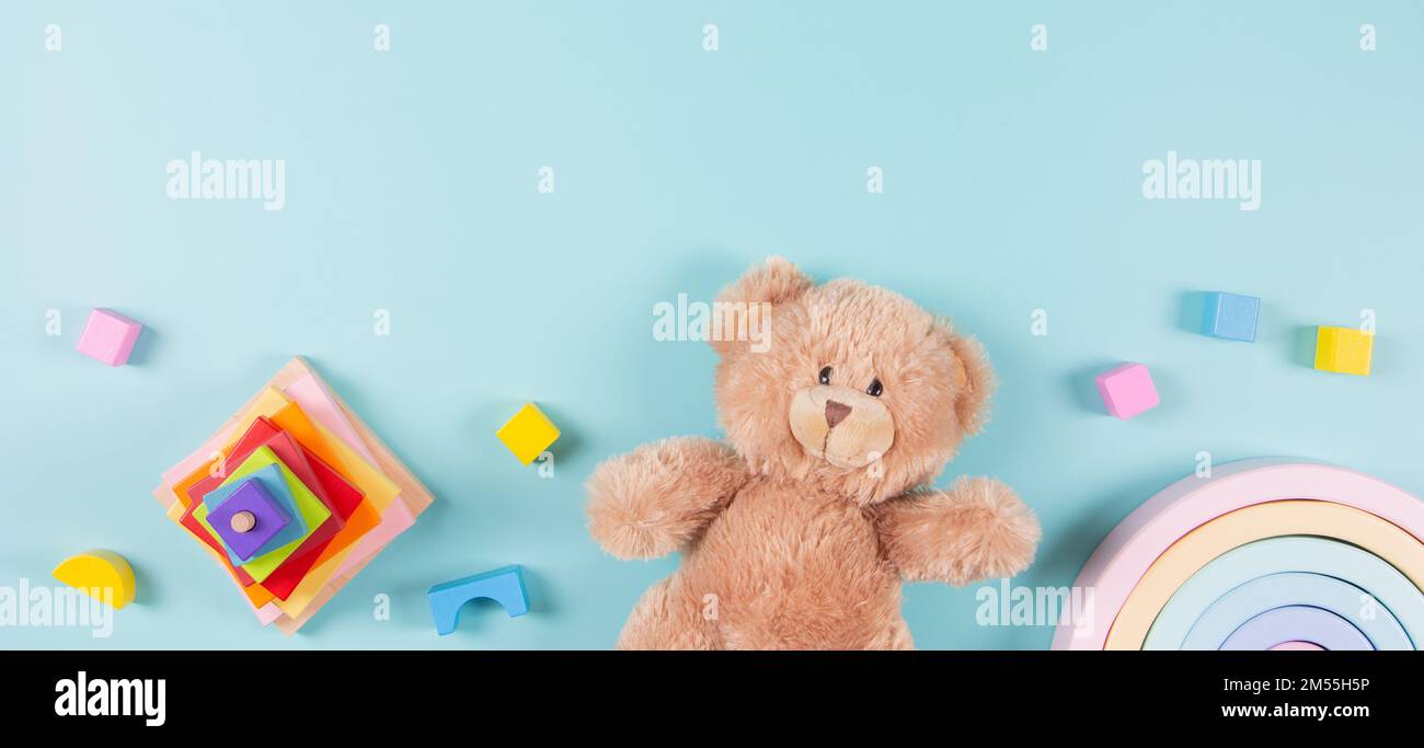 Hintergrund für Lernspielzeug für Babys und Kinder. Teddybär, stapelbarer Pyramidenturm aus Holz, Spielzeugregenbogen und bunte Bausteine auf hellblauem Hintergrund. Oben Stockfoto