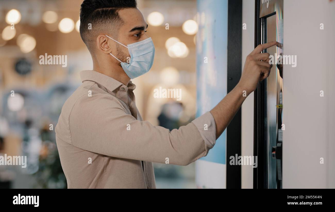 Hispanischer indischer Passagier männlicher Käufer Mann in medizinischer Maske im Flughafen Café berühren Selbstbedienungsautomat beim Kauf des Tickets Online-Bestellung Scroll Touch Stockfoto