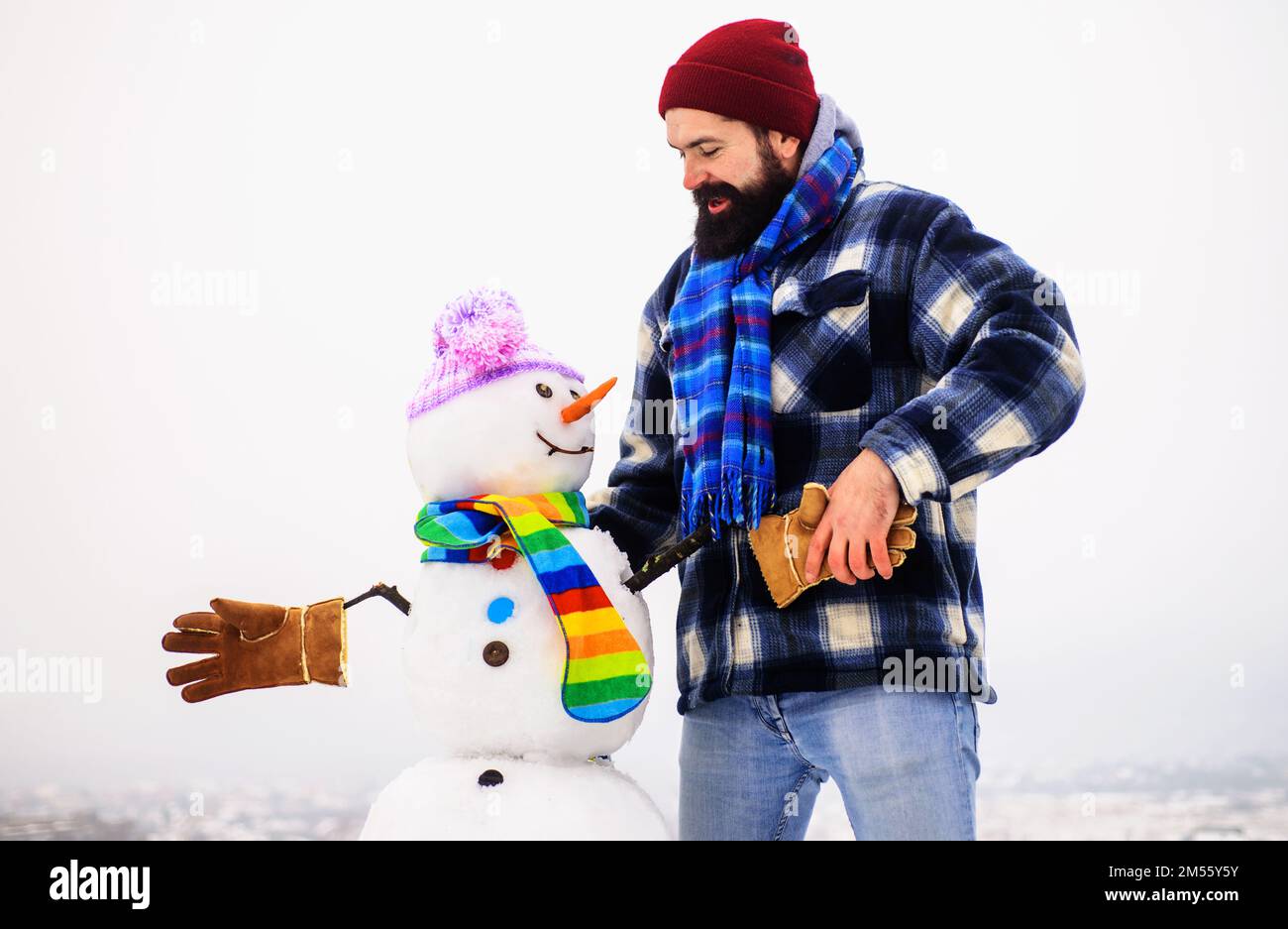 Ein bärtiger Mann in warmer Kleidung schüttelt mit dem Schneemann die Hand. Wintermode. Schneemänner mit Hut, Schal, Handschuhen. Stockfoto