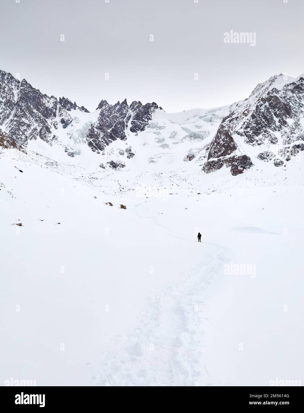 Kleiner Mann mit Rucksack, der auf dem Schneehügel in den wunderschönen Bergen vor dem wolkigen Himmel in Almaty, Kasachstan, spaziert Stockfoto