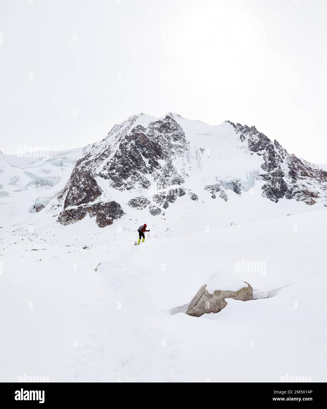 Kleiner Mann mit Rucksack, der auf dem Schneehügel in den wunderschönen Bergen vor dem wolkigen Himmel in Almaty, Kasachstan, spaziert Stockfoto