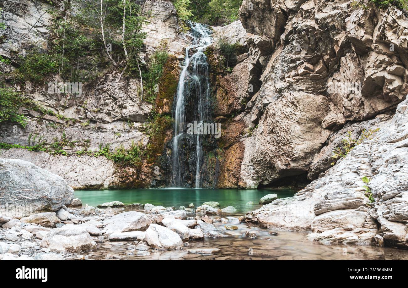 Wunderbarer kleiner Wasserfall, der einen smaragdgrünen Teich in einem Herbstwald bildet Stockfoto