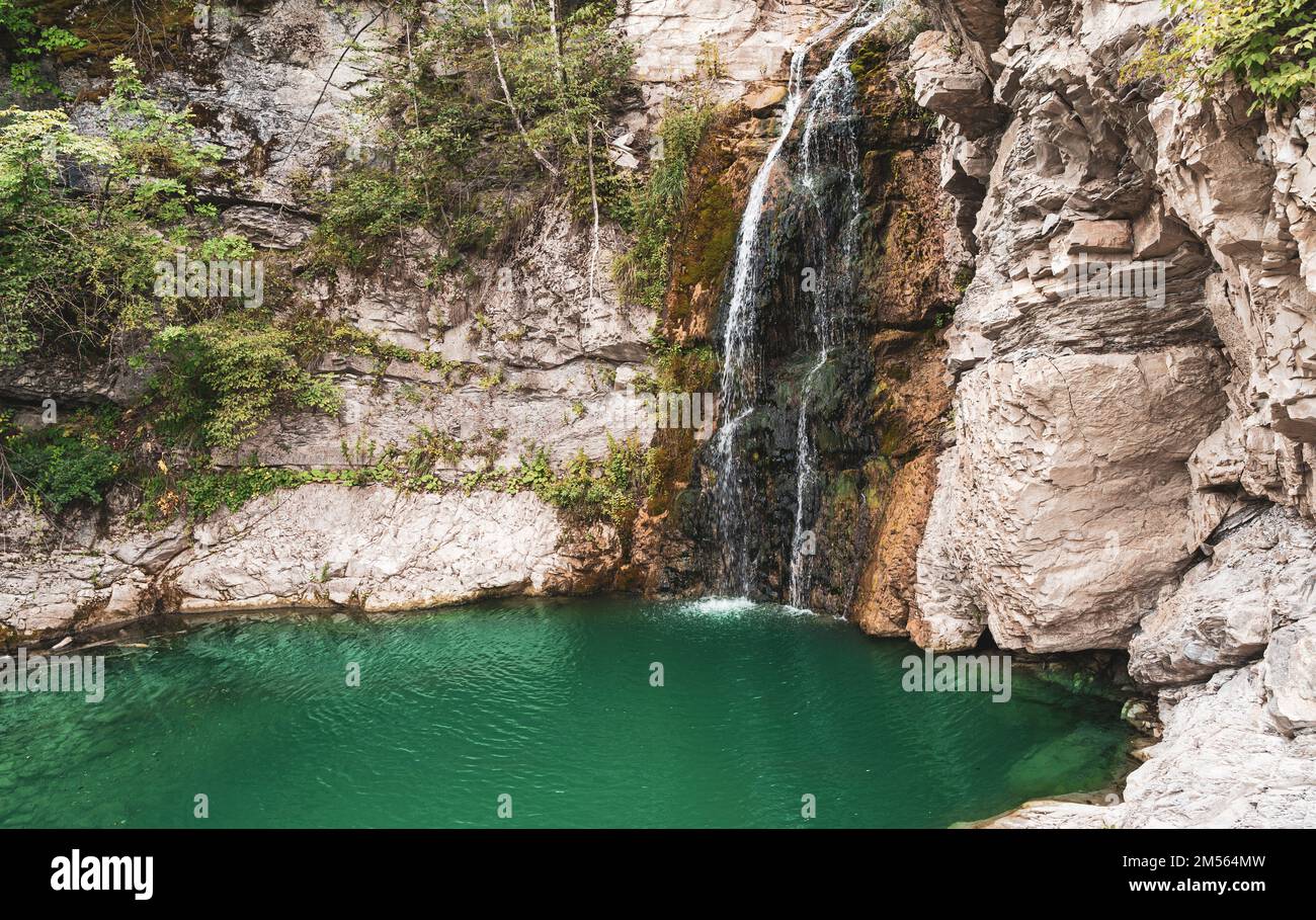 Wunderbarer kleiner Wasserfall, der einen smaragdgrünen Teich in einem Herbstwald bildet Stockfoto