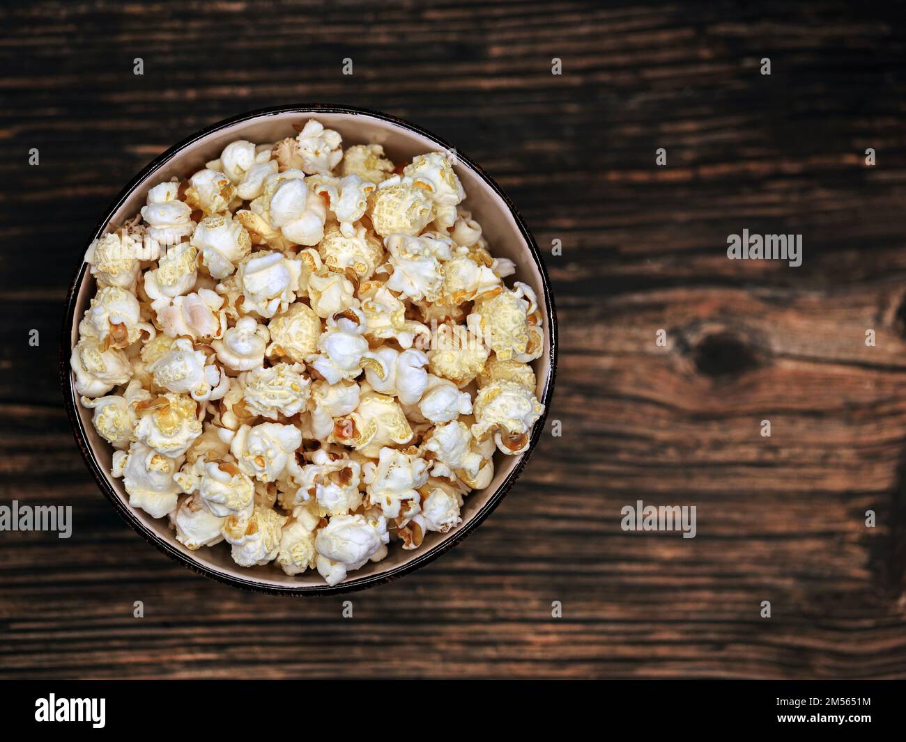 Draufsicht auf Popcorn in der Schüssel auf dunklem Holzhintergrund, Popcorn-Snack auf einem Tisch mit Kopierbereich Stockfoto