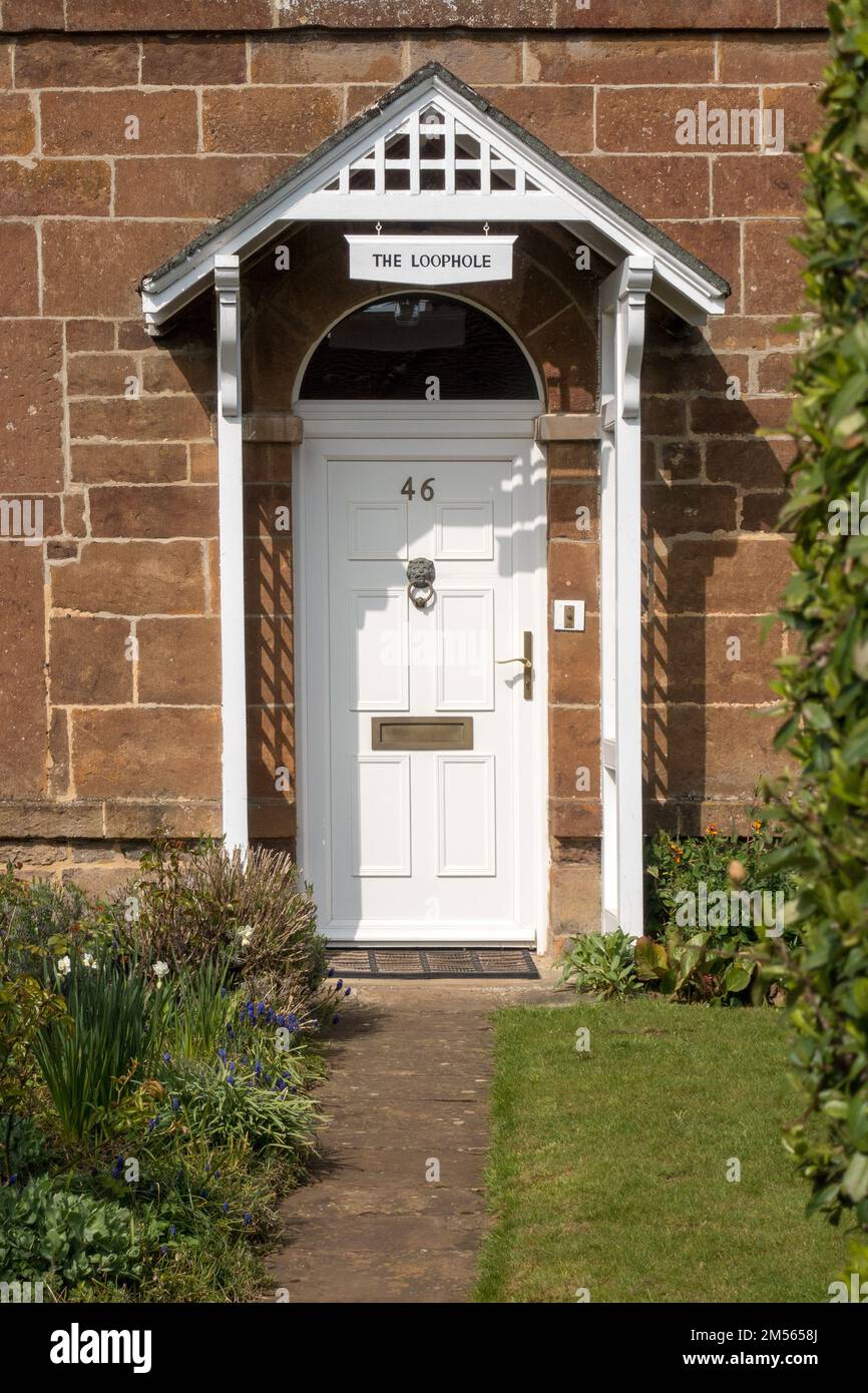 Attraktive, weiß bemalte Haustür mit Steinwänden, kunstvoll verzierte Holzveranda und Namensschild "The Loophole", Uppingham, Rutland, England, Großbritannien Stockfoto