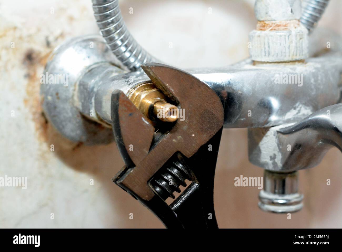 Ein Klempner, der ein Problem mit einem Wasserhahn in der Dusche löst, der den Kartuschenkörper mit einem verstellbaren Schraubenschlüssel dreht, um ihn, die Leitungen und die Wartungskosten zu wechseln Stockfoto