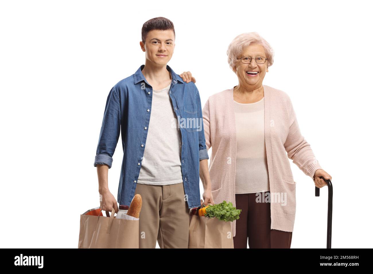 Junger Mann, der einer älteren Frau mit eingedickten Einkaufstaschen auf weißem Hintergrund hilft Stockfoto