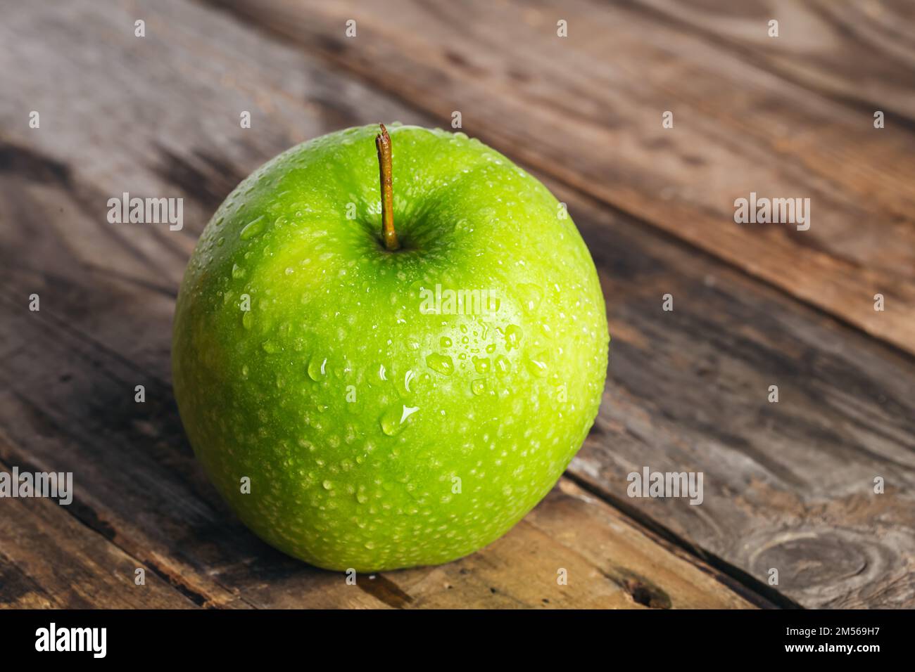Grüner Apfel mit Wassertropfen auf Holzhintergrund Nahaufnahme. Stockfoto