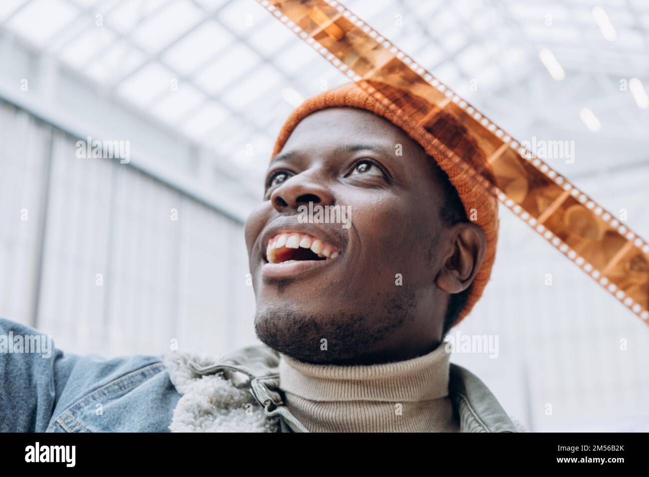 Emotional glücklicher afroamerikanischer Männerfotograf in Denim-Jacke blickt in hell erleuchteter, extremer Nahaufnahme auf Vintage-Film Stockfoto