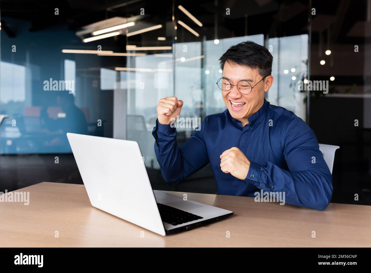 Ein junger asiatischer Student erhielt gute Nachrichten, Post, bestanden die Prüfung, ging zur Universität, erhielt ein Stipendium. Er sitzt im Büro, sieht auf den Monitor, freut sich, zeigt mit seiner Hand Ja Stockfoto