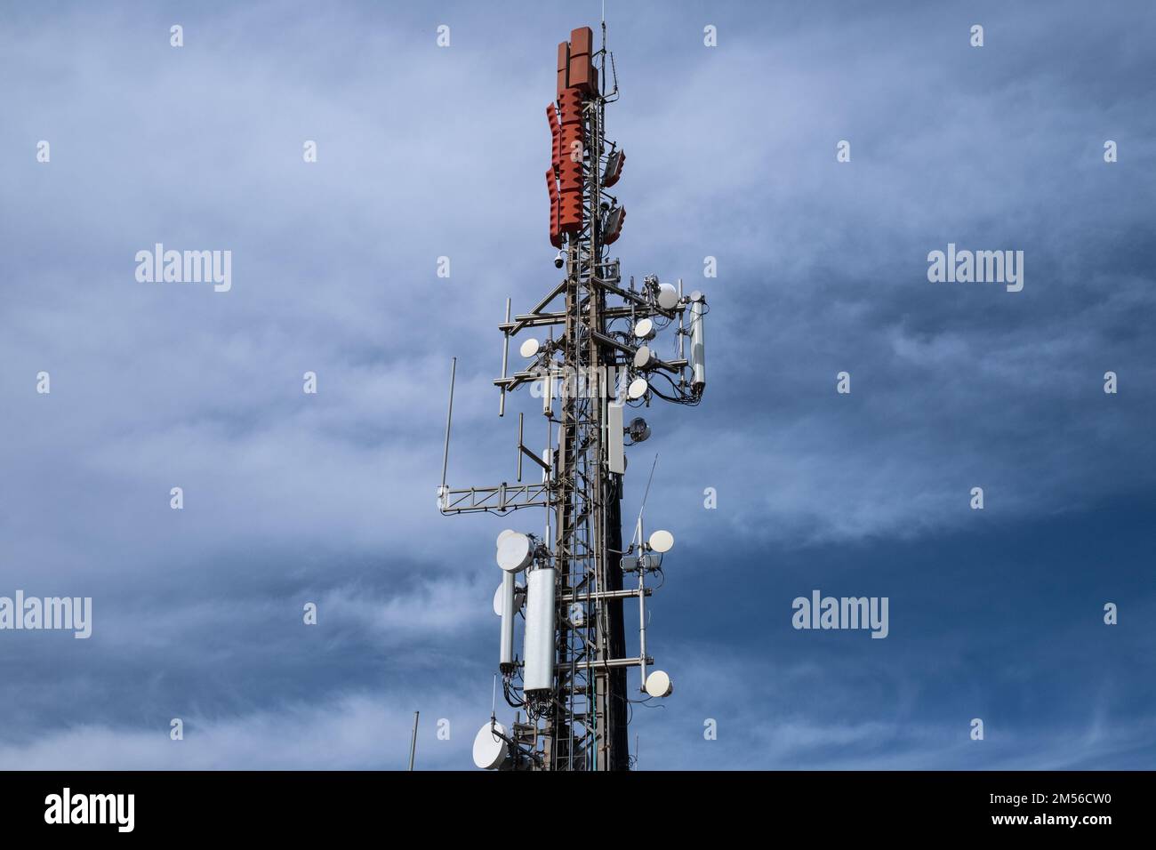 Geringer Blickwinkel auf einen Kommunikationsturm mit Antennen und Sendern gegen bewölkten Himmel. Kommunikationstechnologie und Telekommunikationsindustrie. Stockfoto