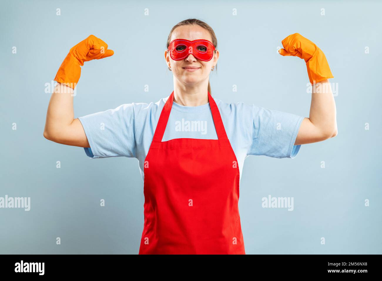 Junge selbstbewusste Hausfrau in der Reinigung von Superheldenkostümen auf blauem Hintergrund Stockfoto