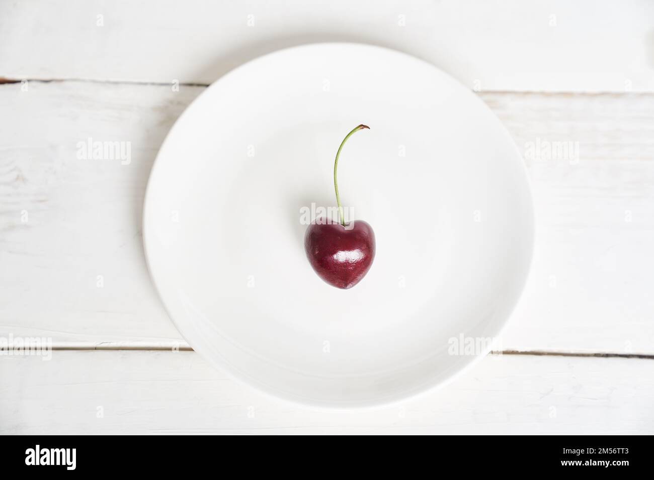 Reife, frische, saftige Beere auf weißem Hintergrund. Eine herzförmige Kirsche auf einem weißen Teller. Fruchthintergrund. valentinstag. Mit einem Platz zum Kopieren. Hochwertiges Foto Stockfoto