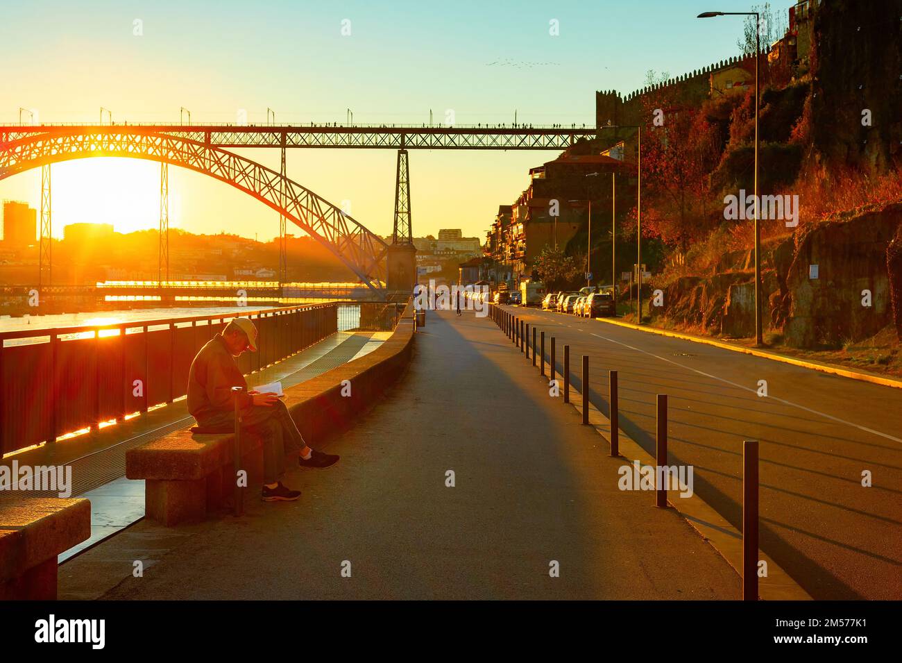 PORTO, PORTUGAL - 21. NOVEMBER 2021: Mann liest Buch über den Ufer bei Sonnenuntergang, Blick auf die Dom Luis Brücke, Porto, Portugal Stockfoto