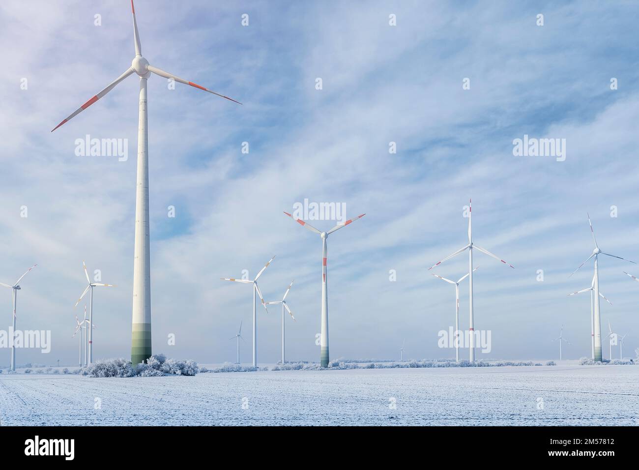 Malerischer Landschaftsblick auf weißes, verschneites, frostiges Feld und große, moderne Windturbinenmühle vor dem wunderschönen blauen Himmel. Ganzjährig sauberes Grün Stockfoto